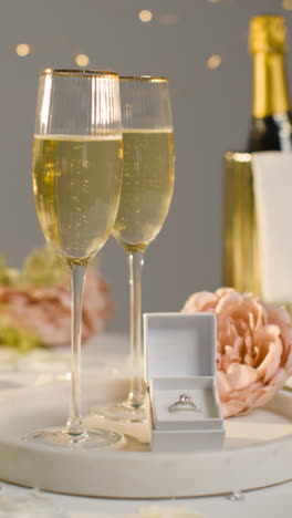 Vertical-Video-Of-Table-Set-For-Romantic-Marriage-Proposal-With-Champagne-And-Engagement-Ring-In-Box